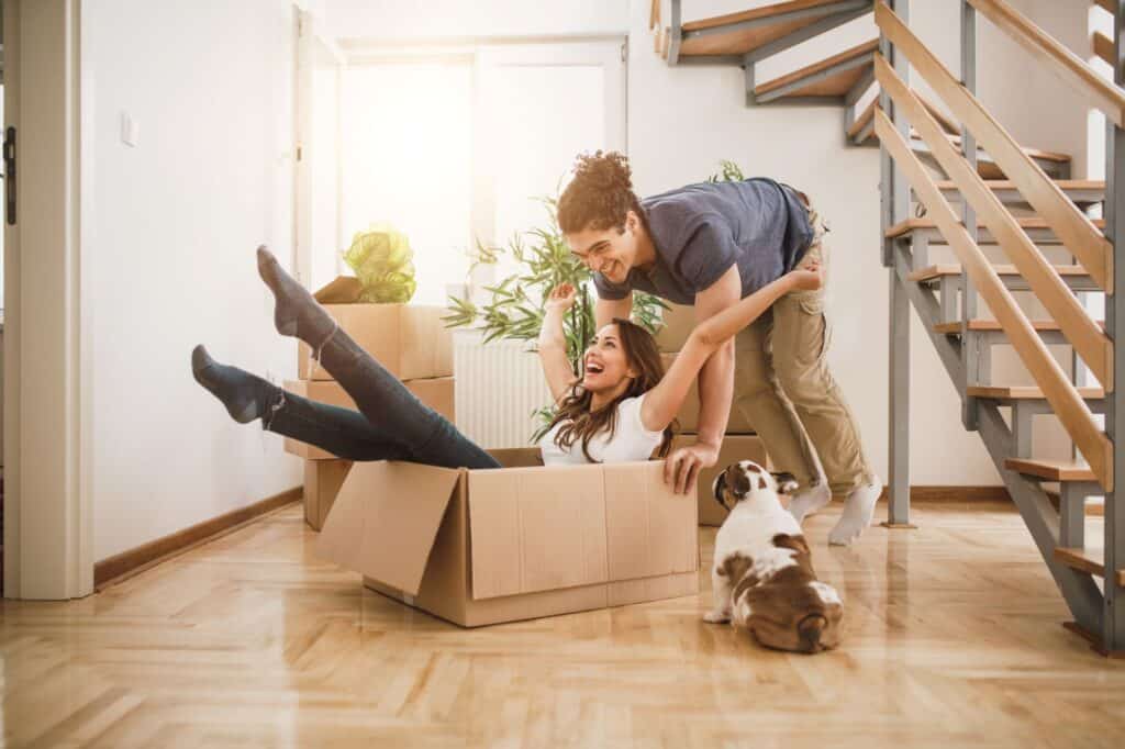 A couple and their pet in their new house full of empty cardboard boxes